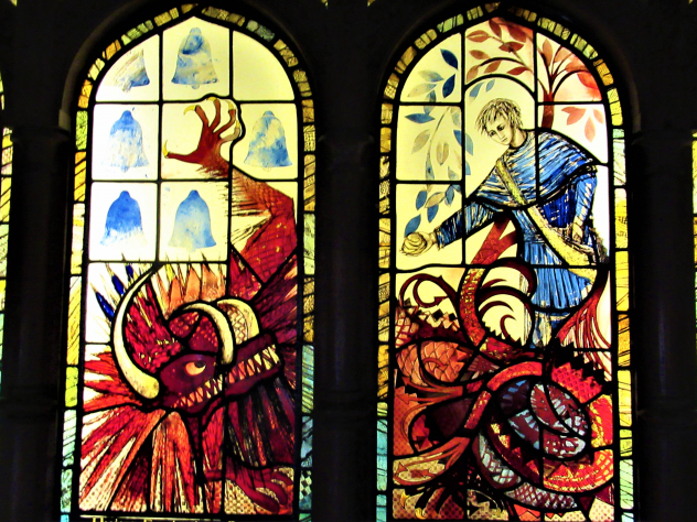 Stained glass windows of a man presenting a lumpy pie to a red dragon.